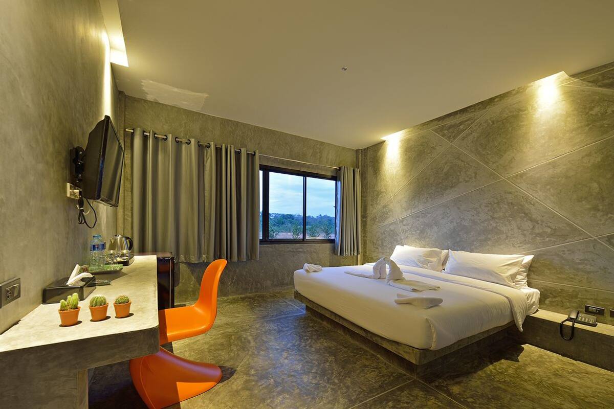 A modern hotel room with a bed, a desk, a chair, a window, and a view of the outdoors.