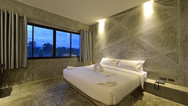 A modern hotel room with a large bed, a view of the outdoors, and a phone on the bedside table. - The Oasis Resort (Krabi)