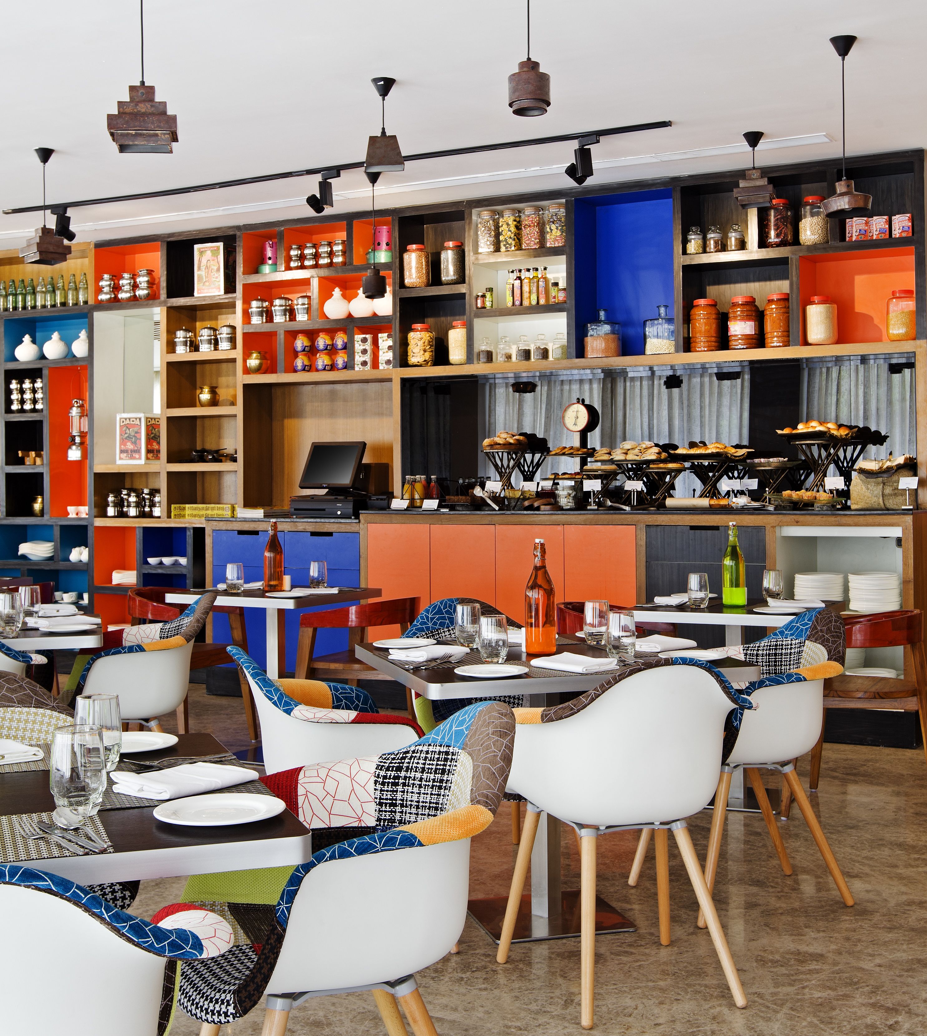 L’intérieur d’un restaurant, avec plusieurs tables et chaises, une caisse enregistreuse et des étagères remplies de pots et de bouteilles.