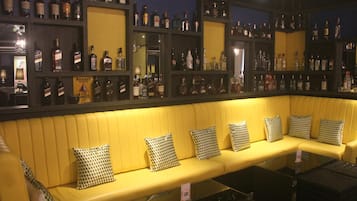 A bar area with a yellow cushioned bench, checkered pillows, and shelves of liquor bottles.