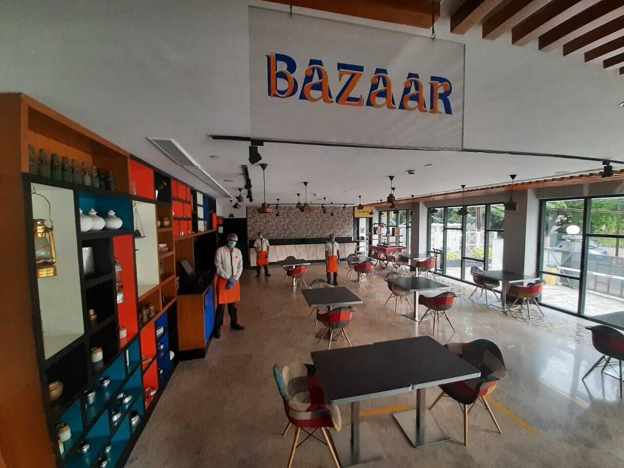 Interior de un restaurante con un letrero 'BAZAAR', mesas, sillas y estanterías con utensilios de cocina.