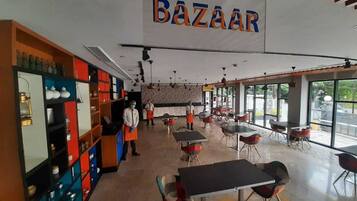 Interior de un restaurante con un letrero 'BAZAAR', mesas, sillas y estanterías con utensilios de cocina.