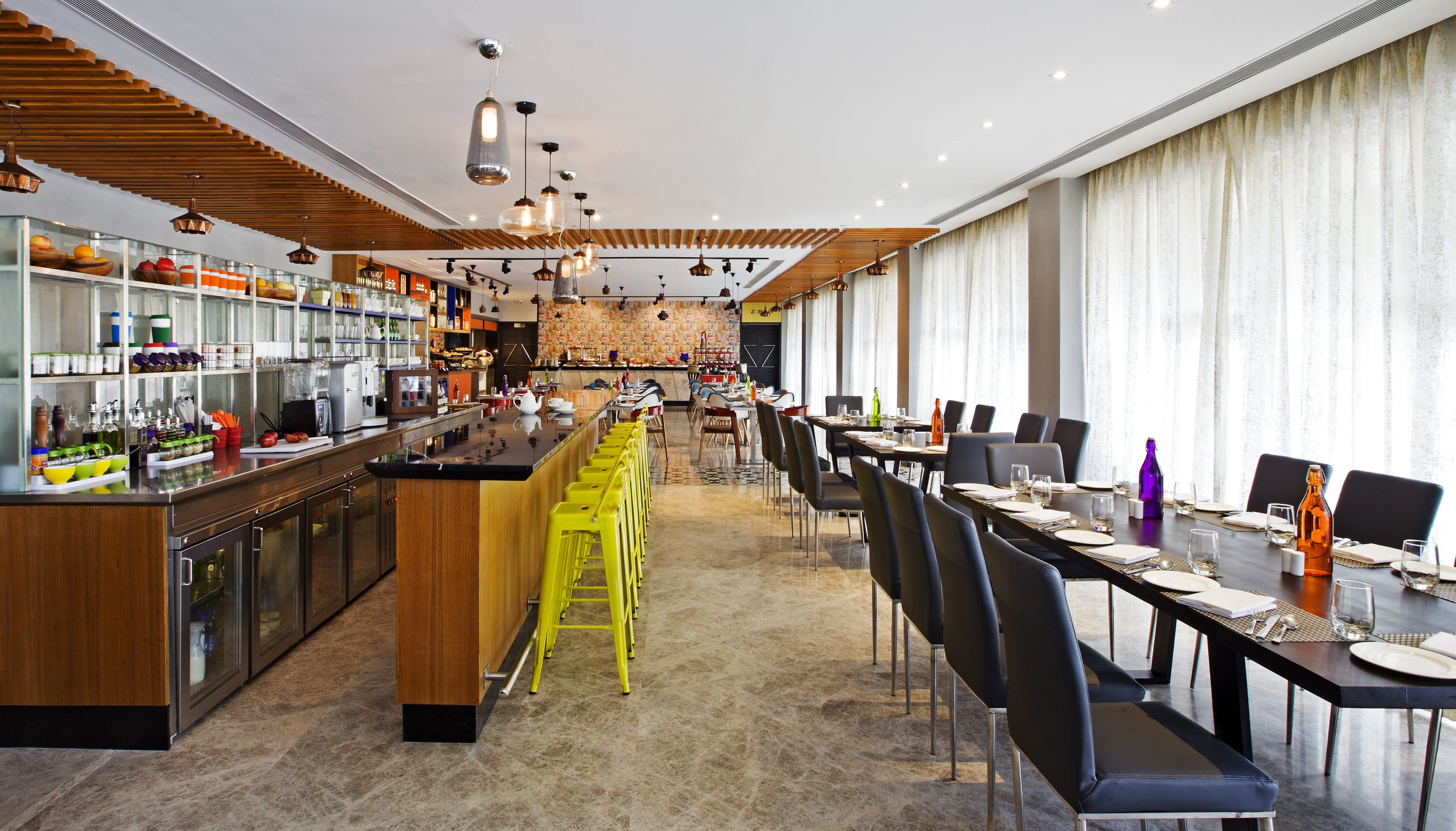A modern restaurant with a bar area, high chairs, and a long dining table.