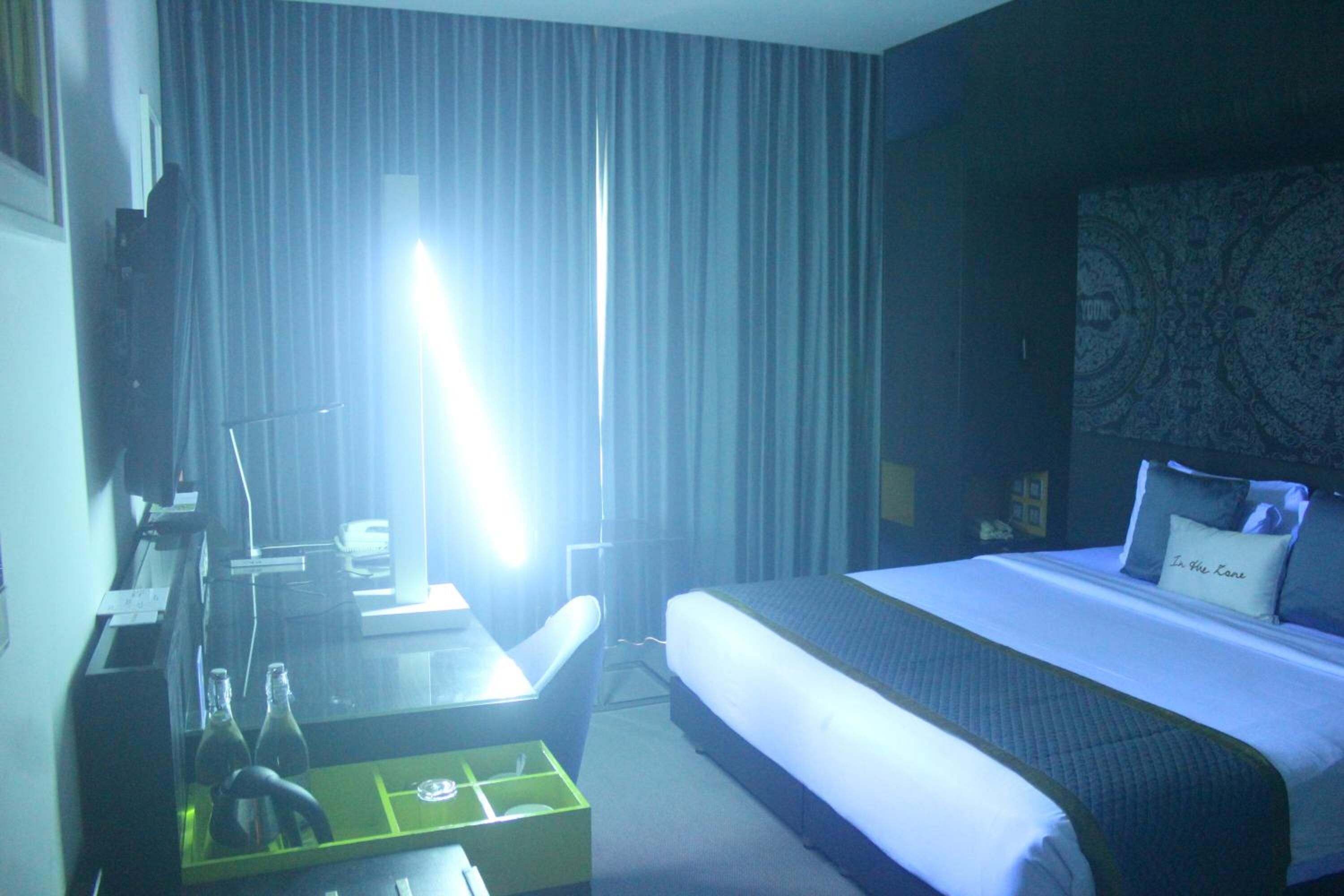 A hotel room with a bed, a desk with a chair, a television, and a window with curtains.