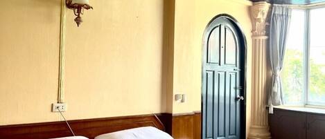 A hotel room with a large bed, a wall-mounted light fixture, a window with curtains, and a door with a decorative arch.