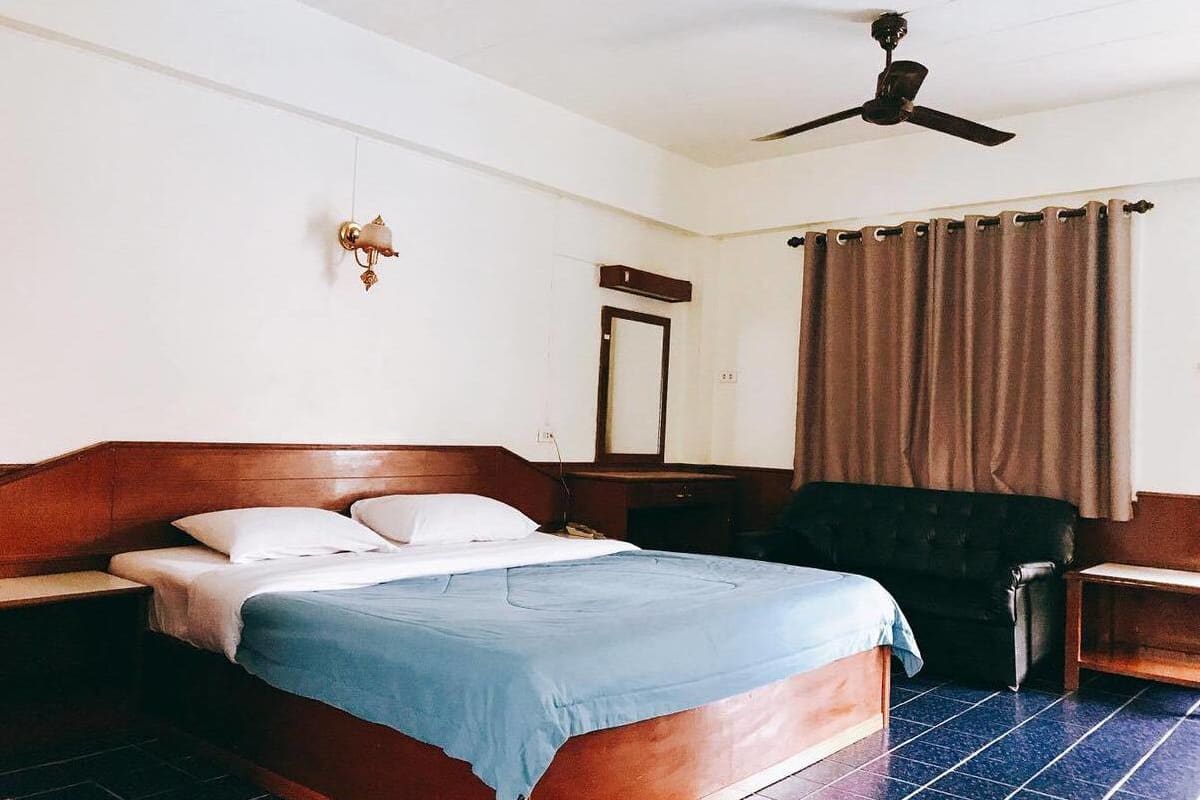 Un dormitorio con cama de madera, mesita de noche, escritorio, ventilador de techo y ventana con cortinas.