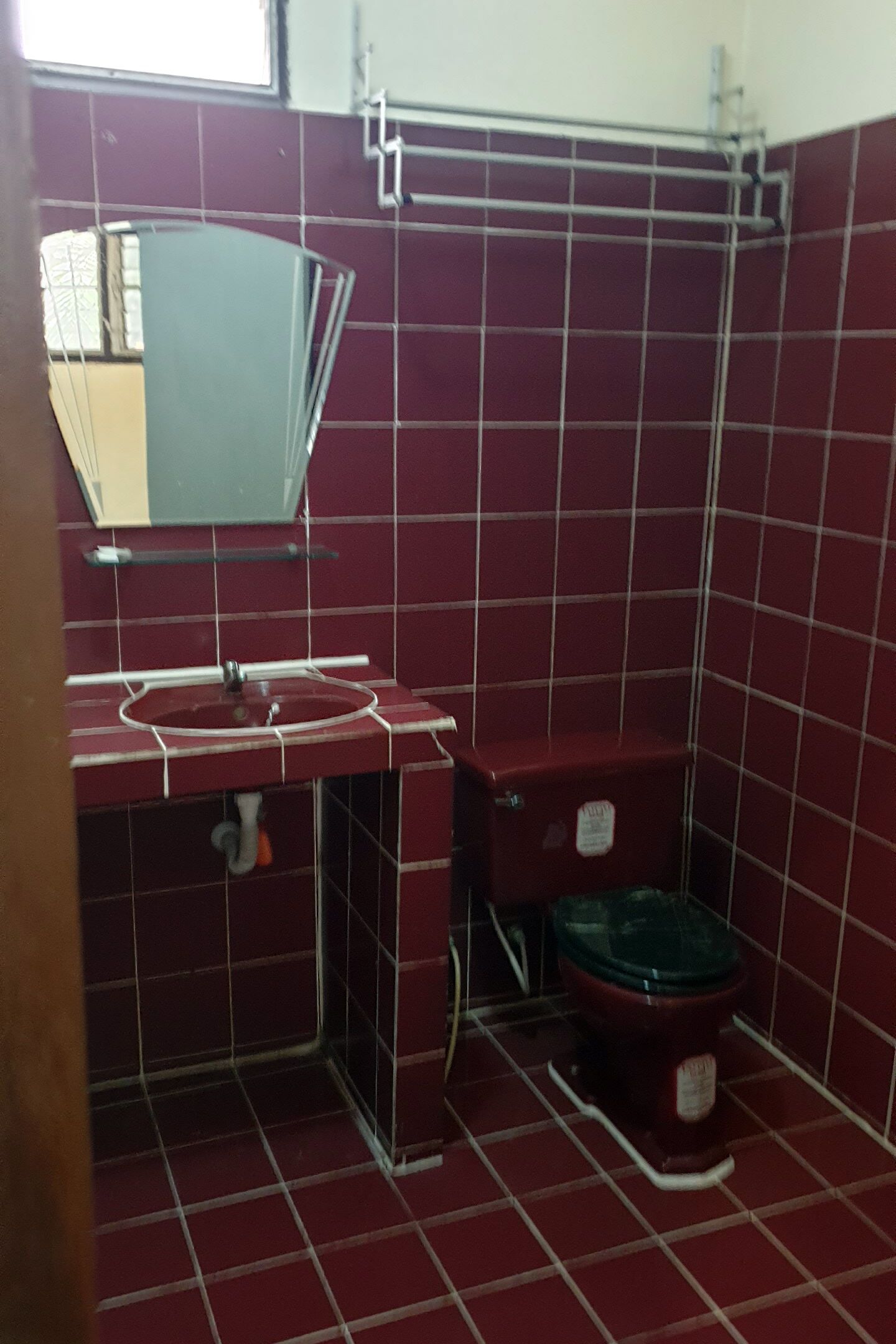 A bathroom with a red tiled floor, a sink, a mirror, and a toilet.