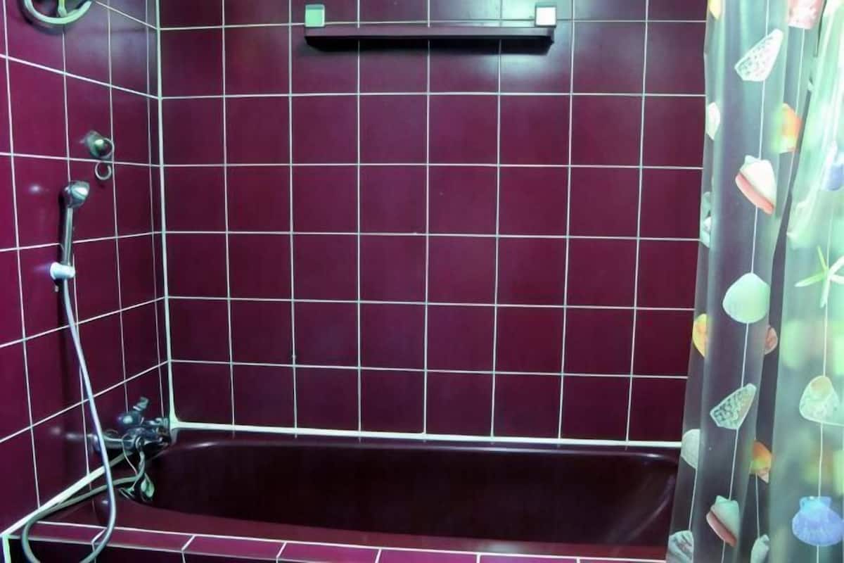 Un baño con una bañera de color oscuro, paredes con azulejos y un cabezal de ducha.