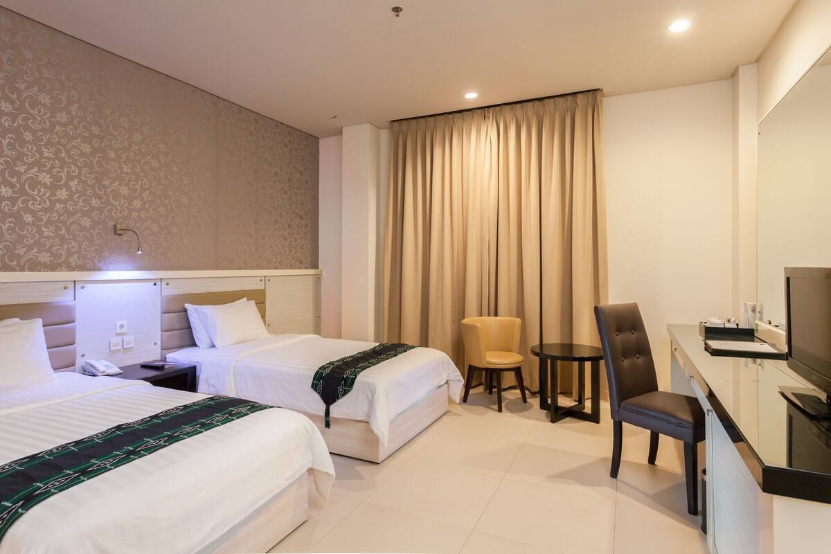 A hotel room with two beds, a desk with a chair, a TV, and a small table with a chair.