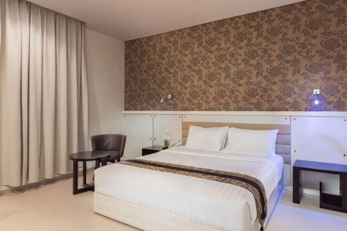 A hotel room with a bed, a chair, a small table, and a nightstand.