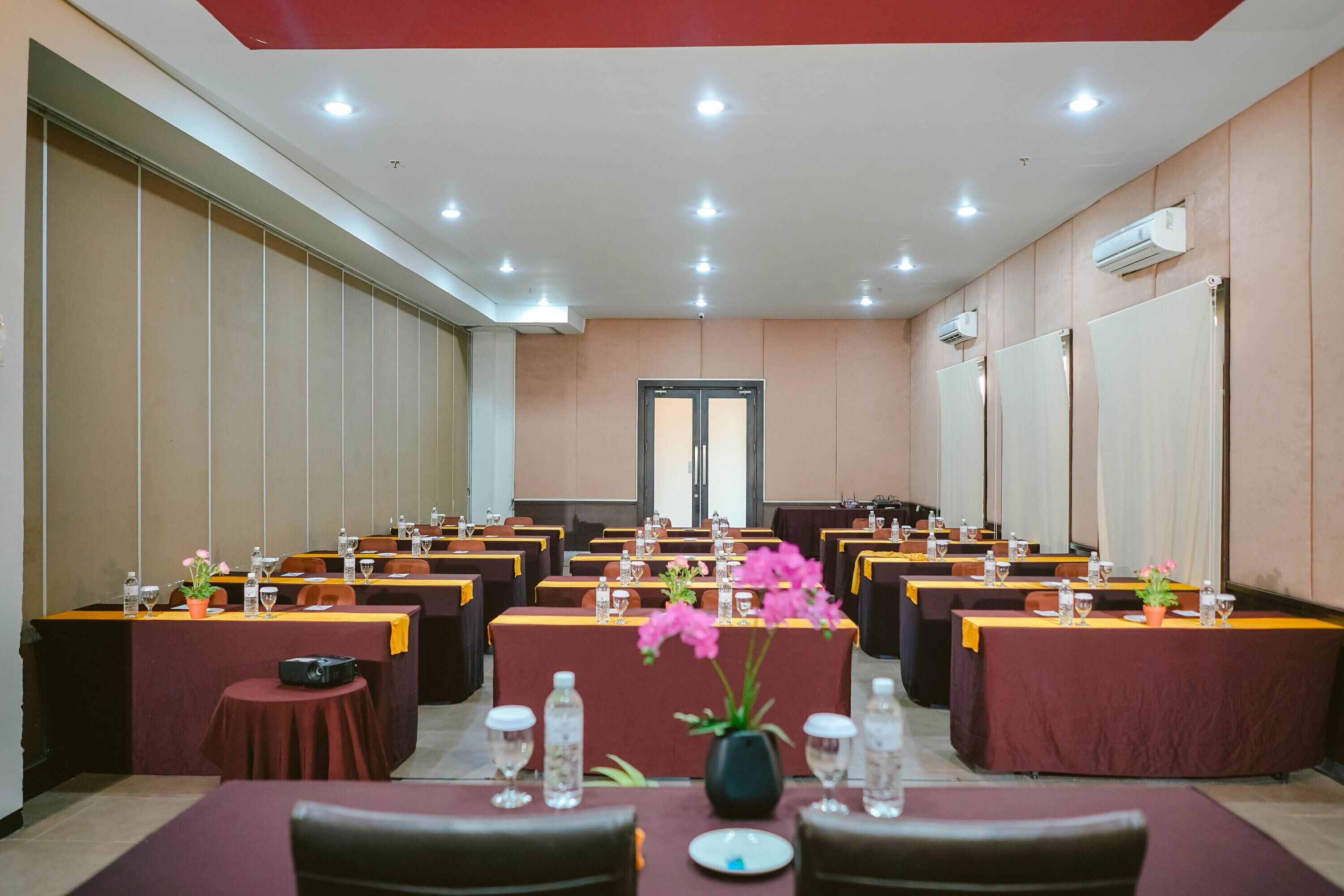 A conference room with multiple tables, each with water bottles, glasses, and vases with flowers.