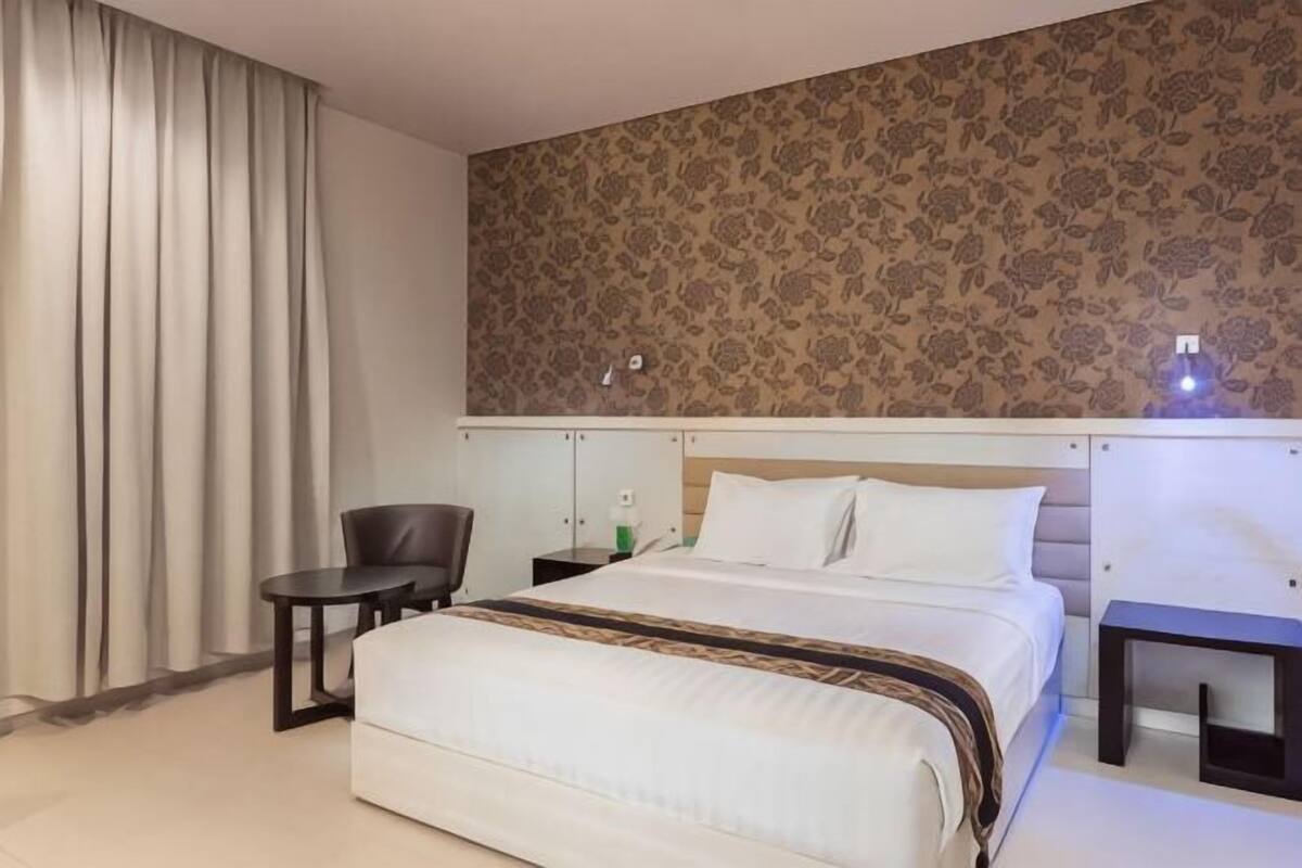 A hotel room with a bed, a chair, a small table, and a nightstand.
