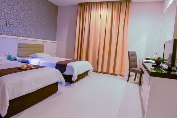 A hotel room with two beds, a desk, a chair, and a television.