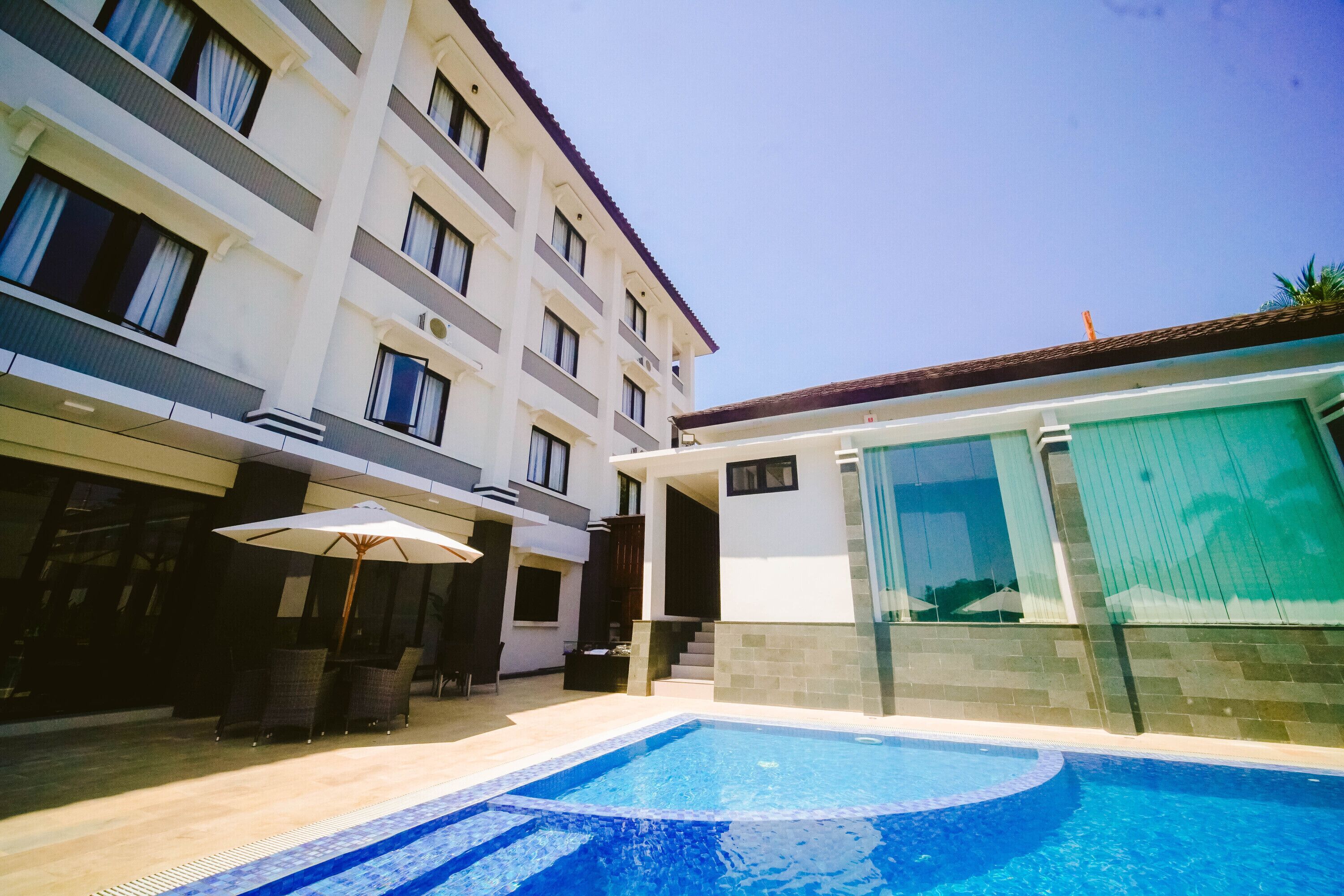 A hotel with a swimming pool, outdoor seating, and a covered patio area.