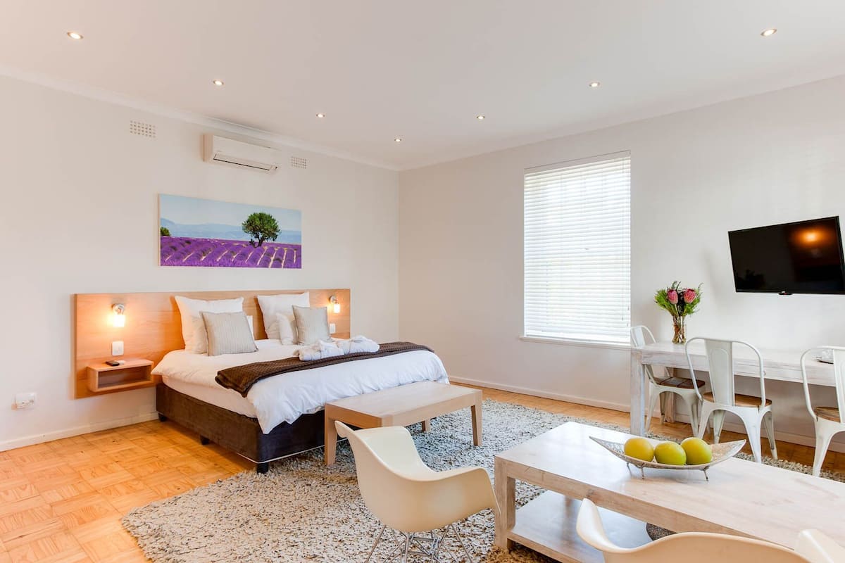 Ein modernes Schlafzimmer mit einem Bett, Nachttischen, einem Schreibtisch mit Stühlen, einem Fernseher und einem Bild an der Wand.