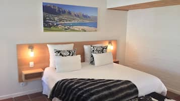 Una camera da letto con un letto, due comodini, una lampada a parete e un dipinto di un paesaggio costiero.
