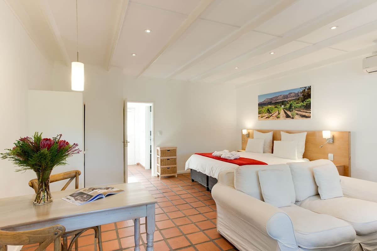 Ein Hotelzimmer mit Bett, Sofa, Esstisch und Blumen in einer Vase.