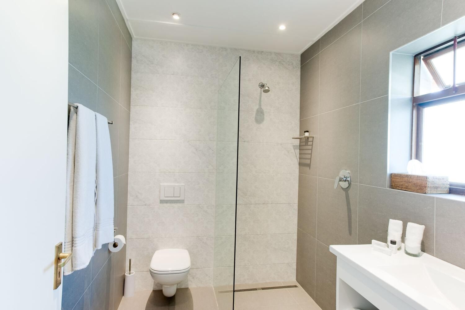 A modern bathroom with a glass-enclosed shower, a toilet, and a sink with a mirror.