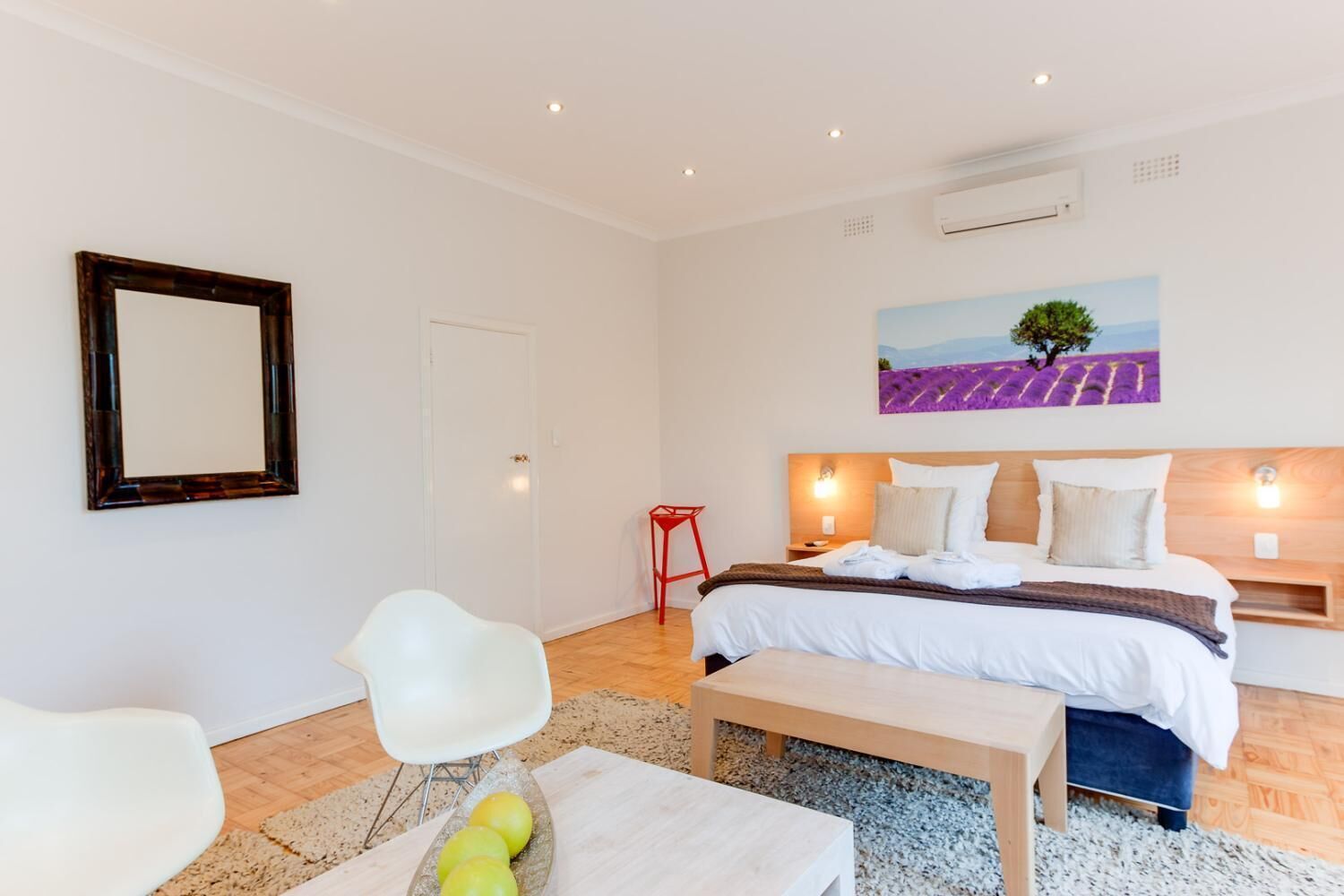 A modern bedroom with a bed, a chair, a table with fruit, and a painting on the wall.