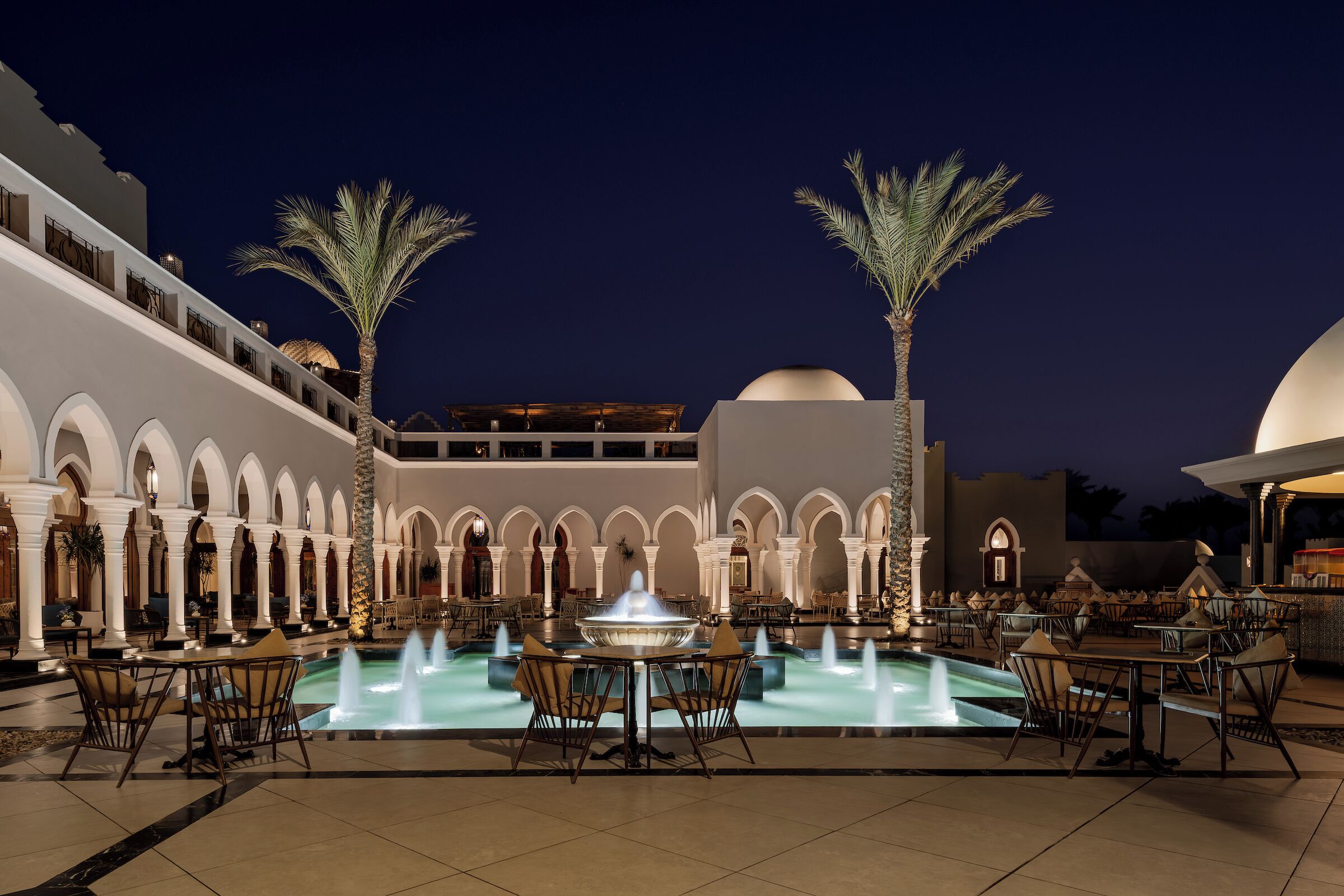 A courtyard with a pool, palm trees, and outdoor seating.