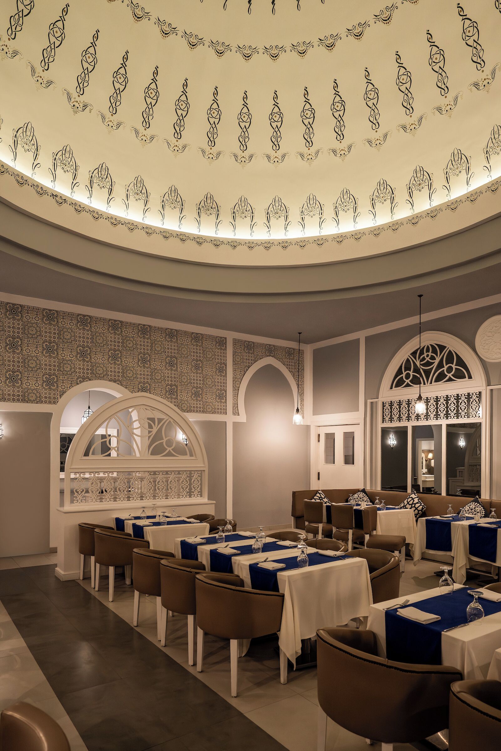 A restaurant with a curved ceiling, patterned wall designs, and tables set for dining.