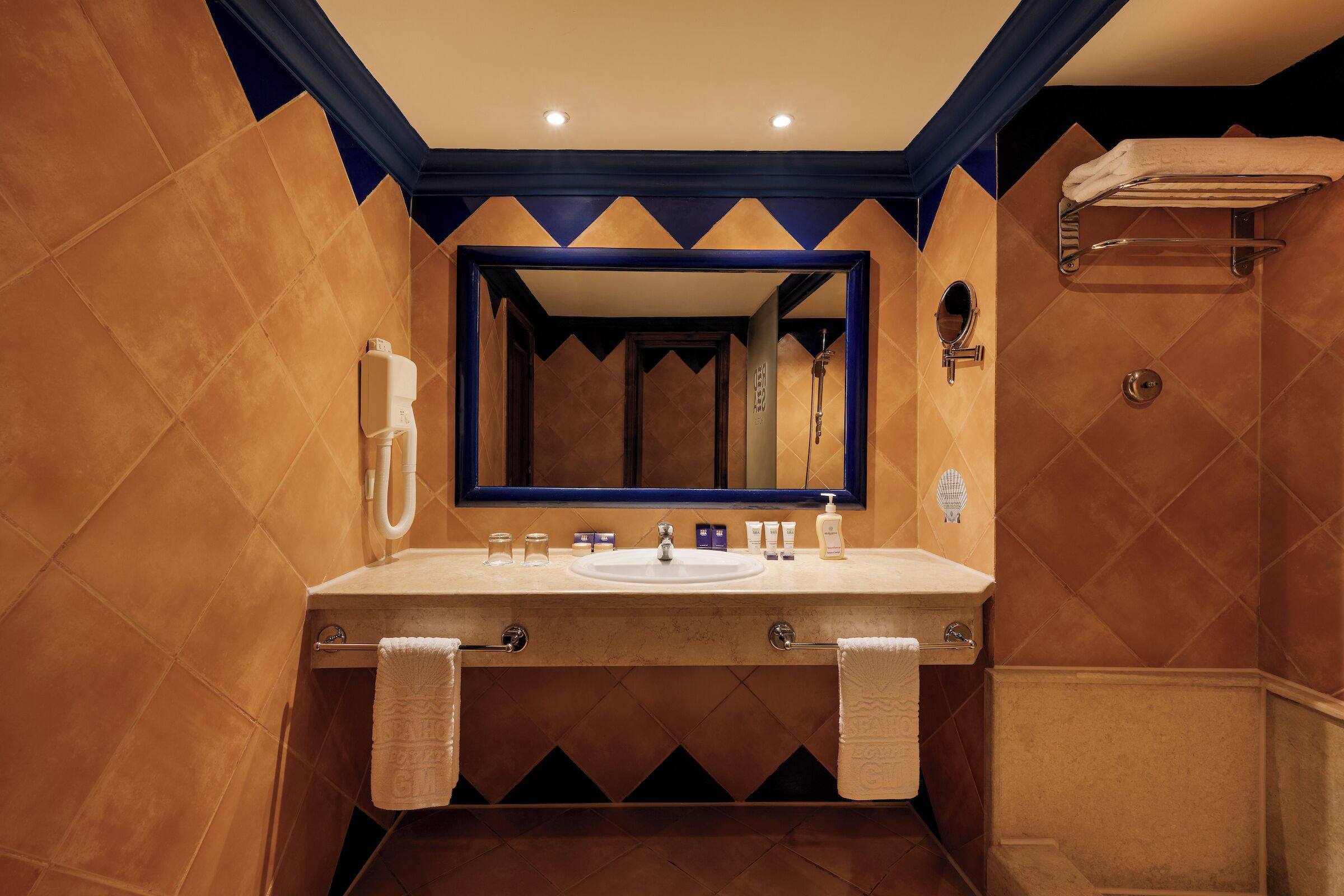 Une salle de bain avec un grand miroir, un lavabo et un porte-serviettes.
