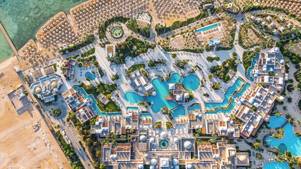 Vue aérienne d’un complexe hôtelier doté de plusieurs piscines, de chaises longues et de palmiers.