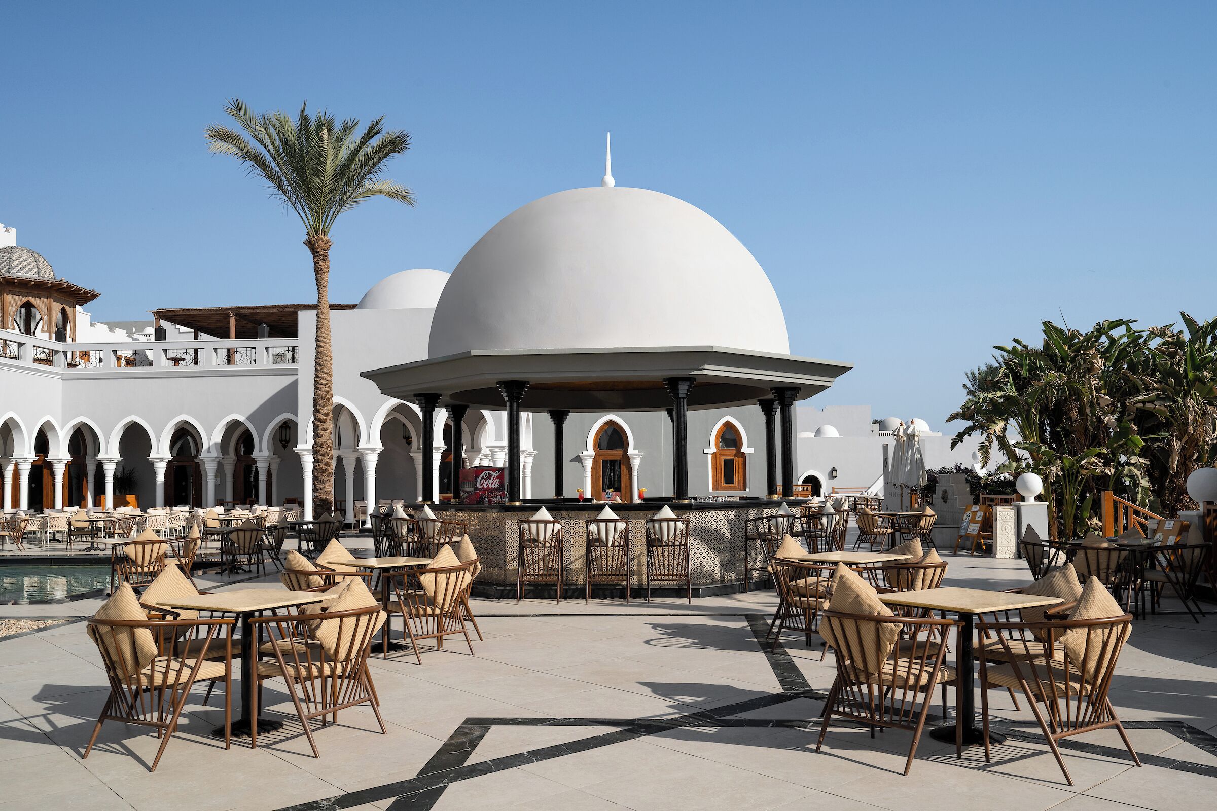 An outdoor dining area with tables and chairs, a pool, and a building with domed architecture.