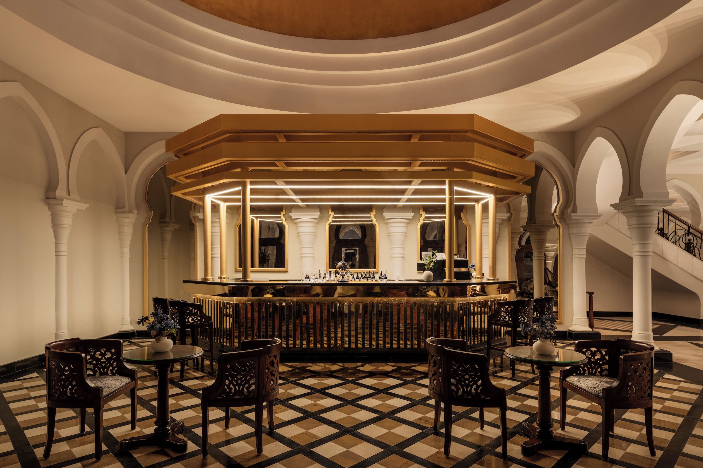 A bar area with a checkered floor, white columns, and ornate chairs.