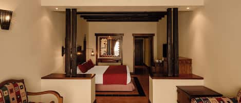 Una habitación de hotel con una cama, dos sillones, un escritorio de madera y un espejo.