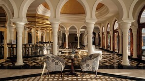 Un hall d’entrée spacieux, doté d’un sol à carreaux, de colonnes blanches et de fauteuils à motifs.