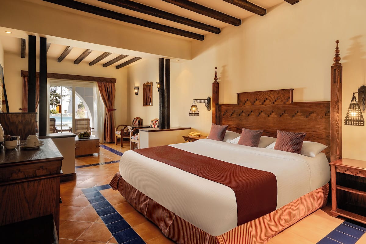 Ruime slaapkamer met een groot bed, houten hoofdeinde en uitzicht op de omgeving.