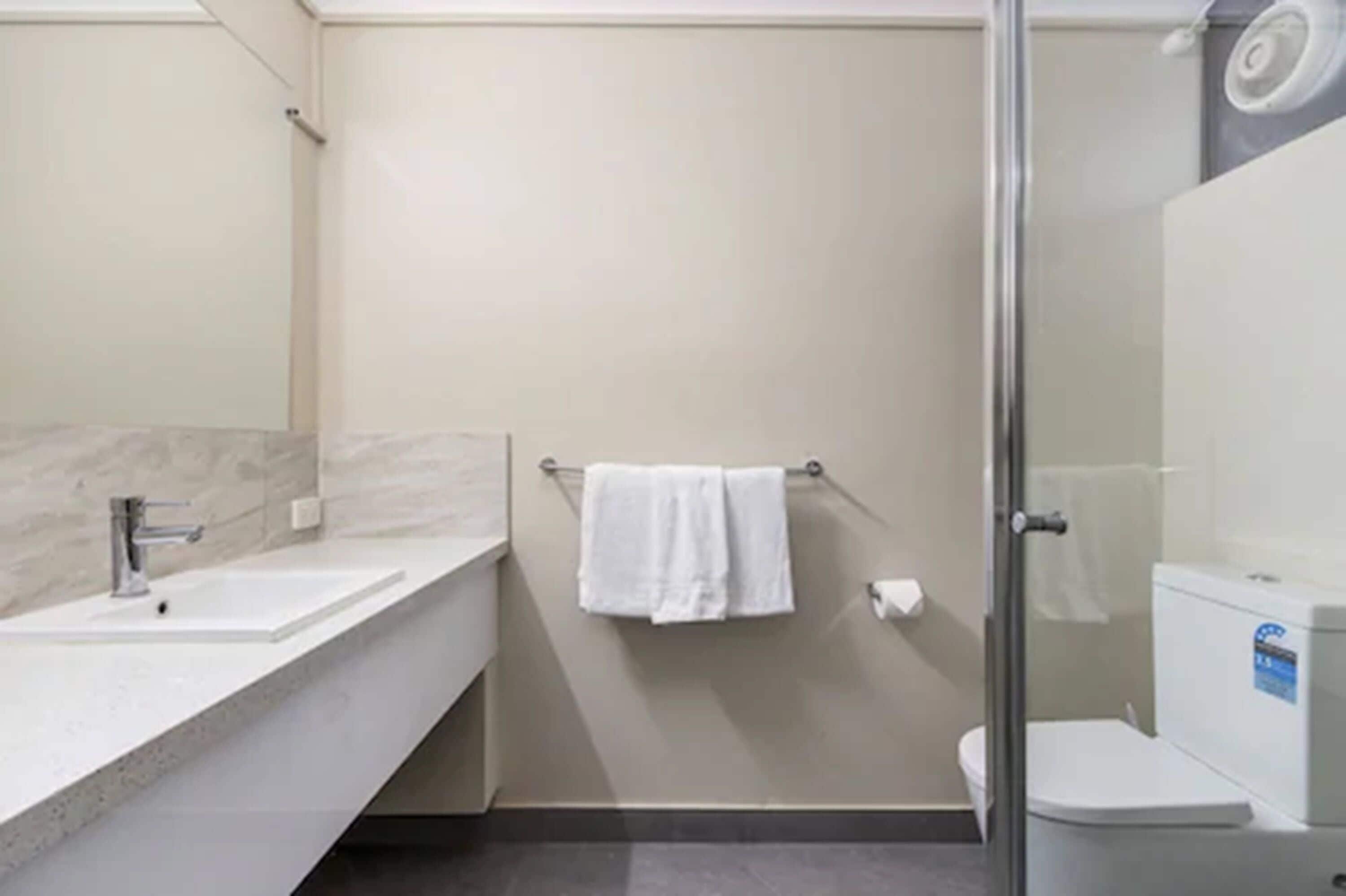 Un baño moderno con cabina de ducha de vidrio, un lavamanos blanco y un inodoro.