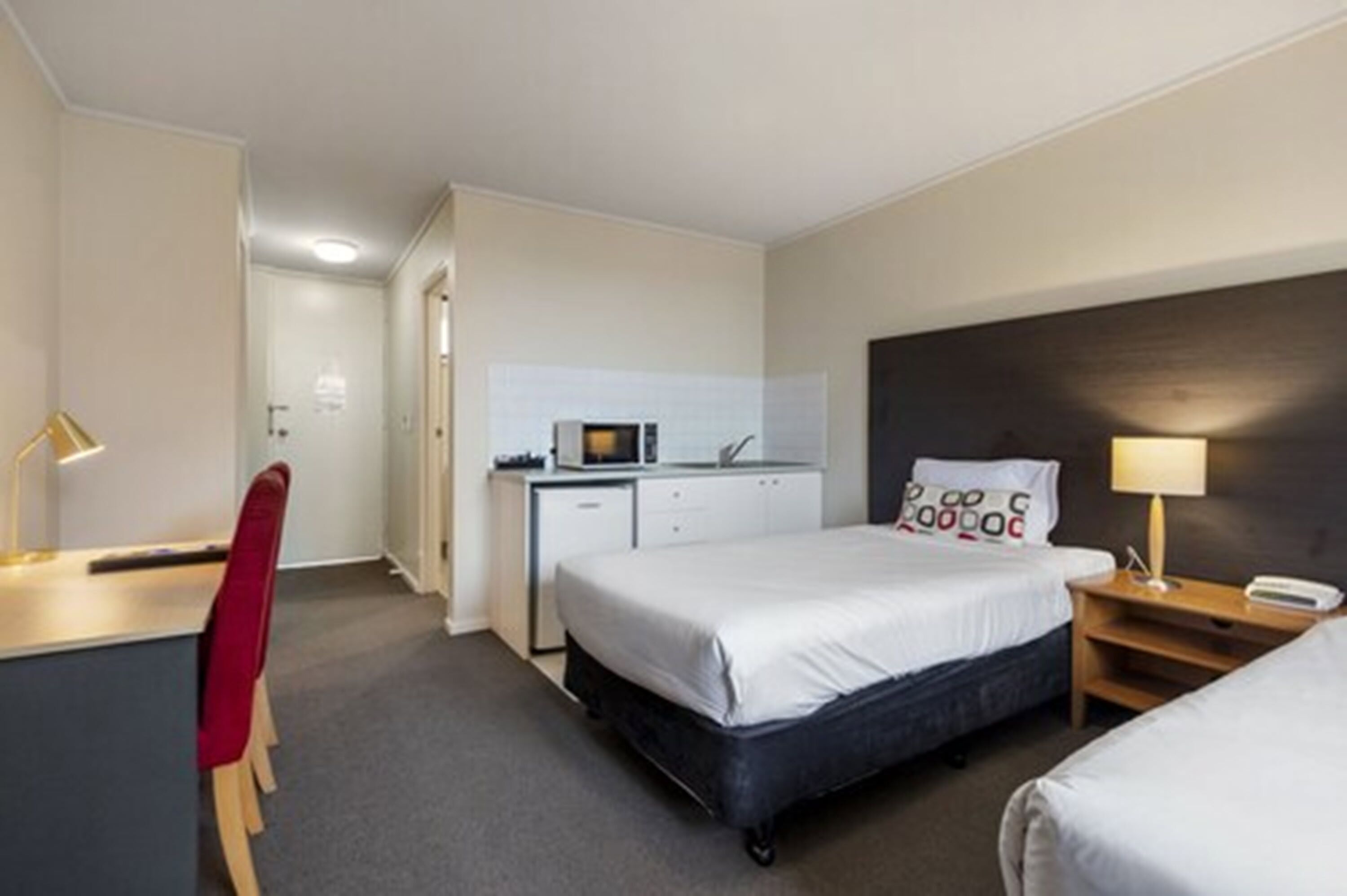 A hotel room with a bed, desk, chair, and a small kitchenette.