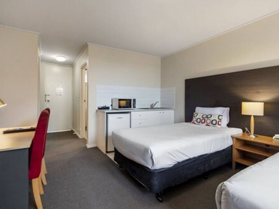 Habitación de hotel con cama, escritorio, silla y una pequeña cocina.