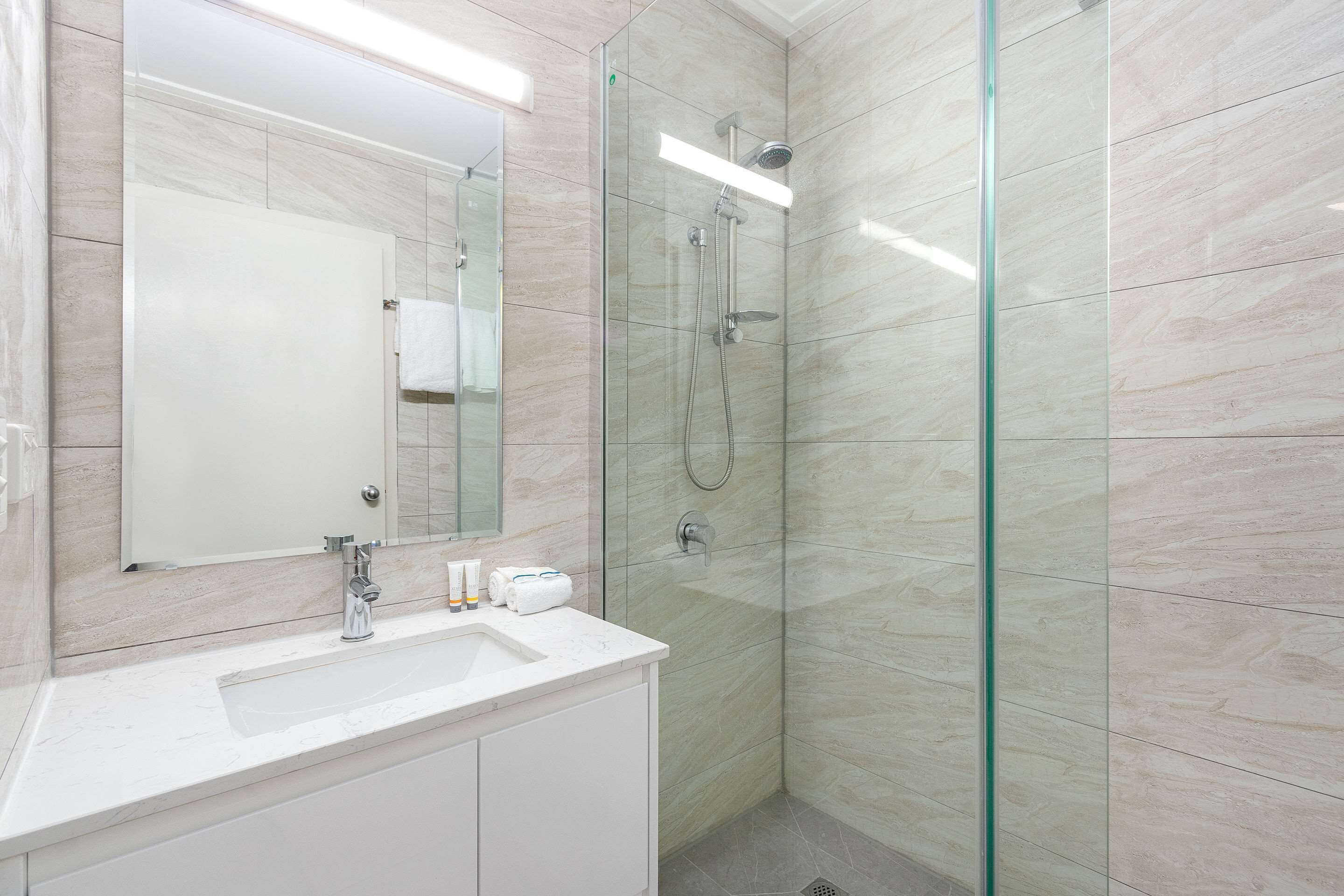 A modern bathroom with a glass-enclosed shower, a white sink, and a large mirror.