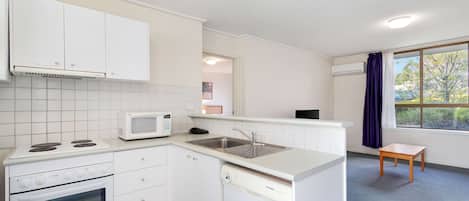 Una cocina compacta con muebles blancos, un microondas, una estufa y un lavavajillas.