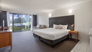 Une chambre avec un grand lit, un bureau, une chaise et un canapé. Il y a une fenêtre qui donne sur un paysage verdoyant.