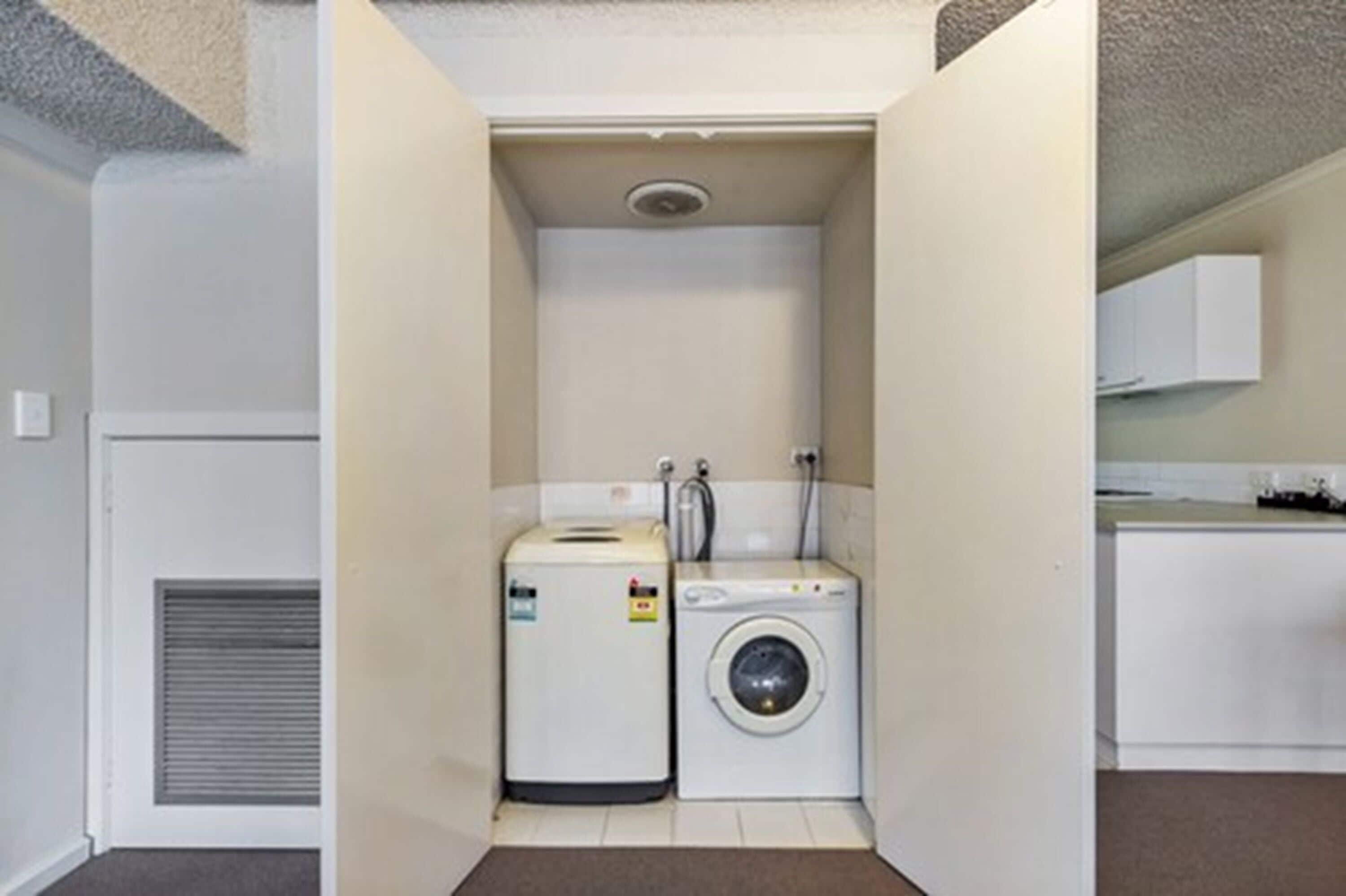 A compact laundry room with a washing machine and a dryer, a small window, and a door leading to another room.