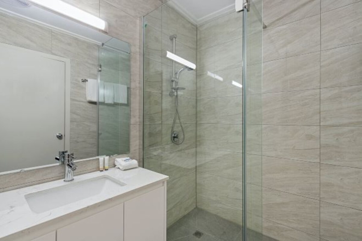 Ein modernes Badezimmer mit einer ein Glasdusche, einem weißen Waschbecken und einem großen Spiegel.