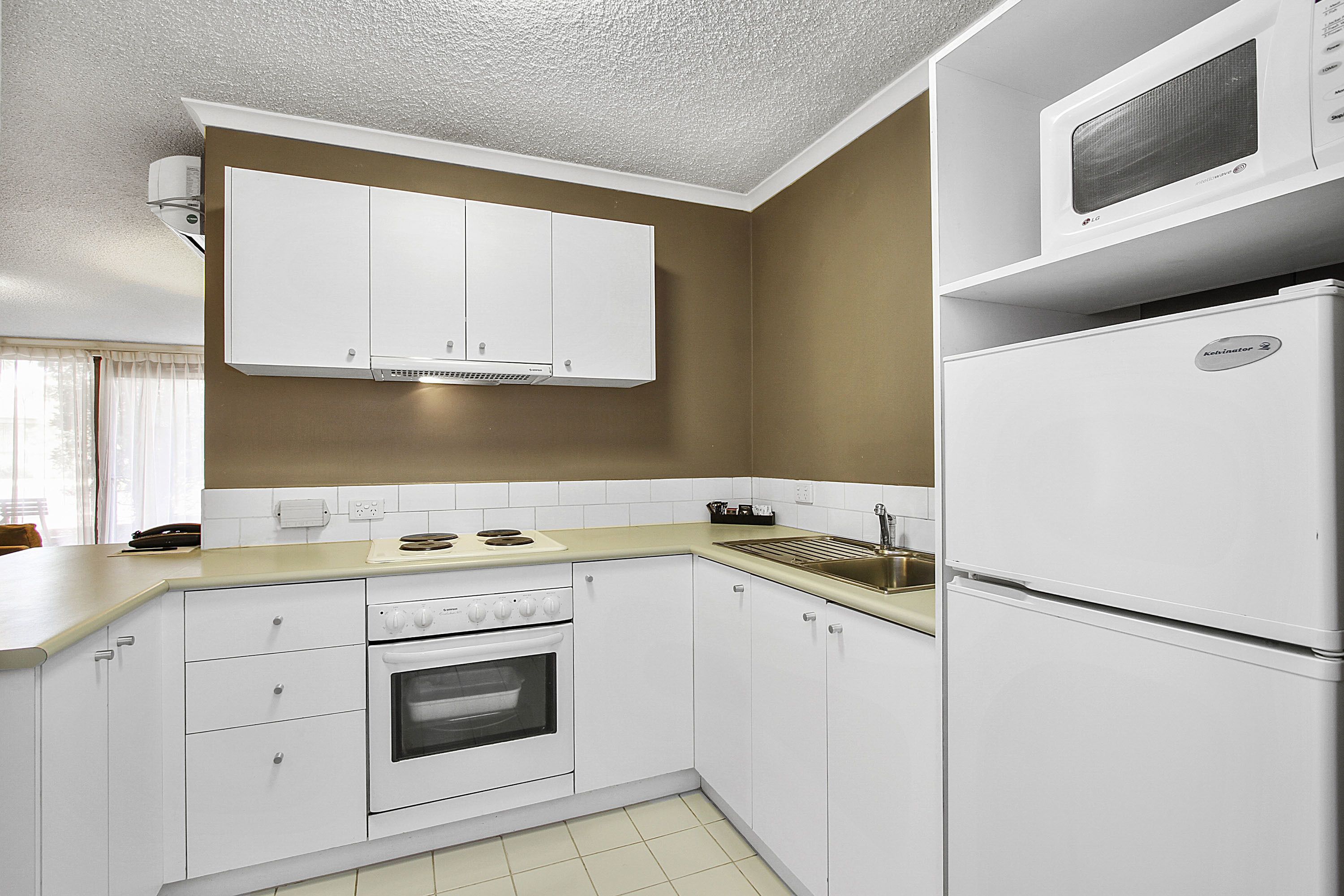 A kitchen with white cabinets, a stove, an oven, a sink, and a microwave.