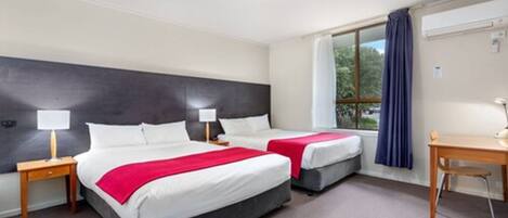 Ein Hotelzimmer mit zwei Betten, einem Schreibtisch und einem Fenster mit Vorhängen.