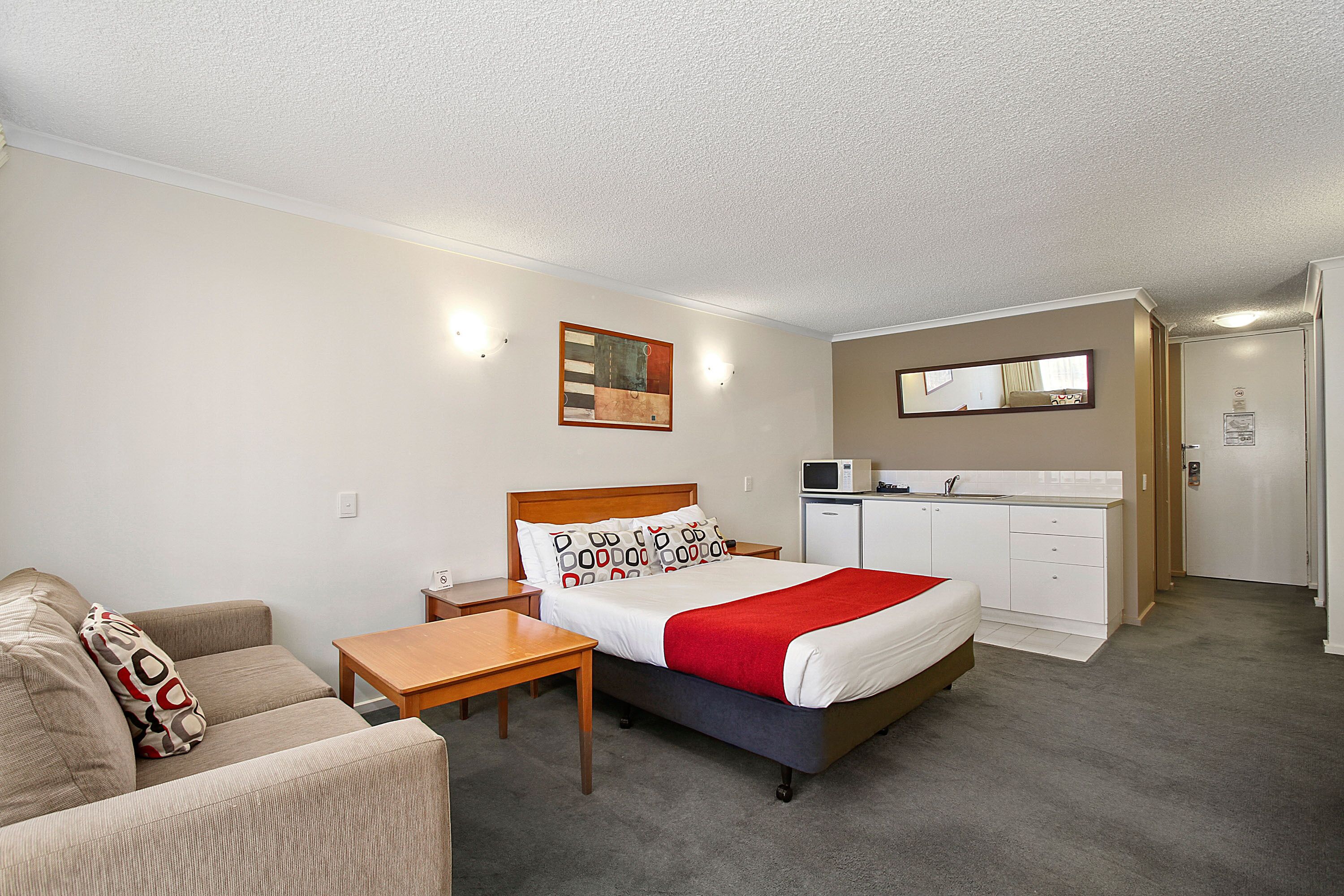 A hotel room with a bed, a sofa, a small table, a microwave, and a kitchenette.