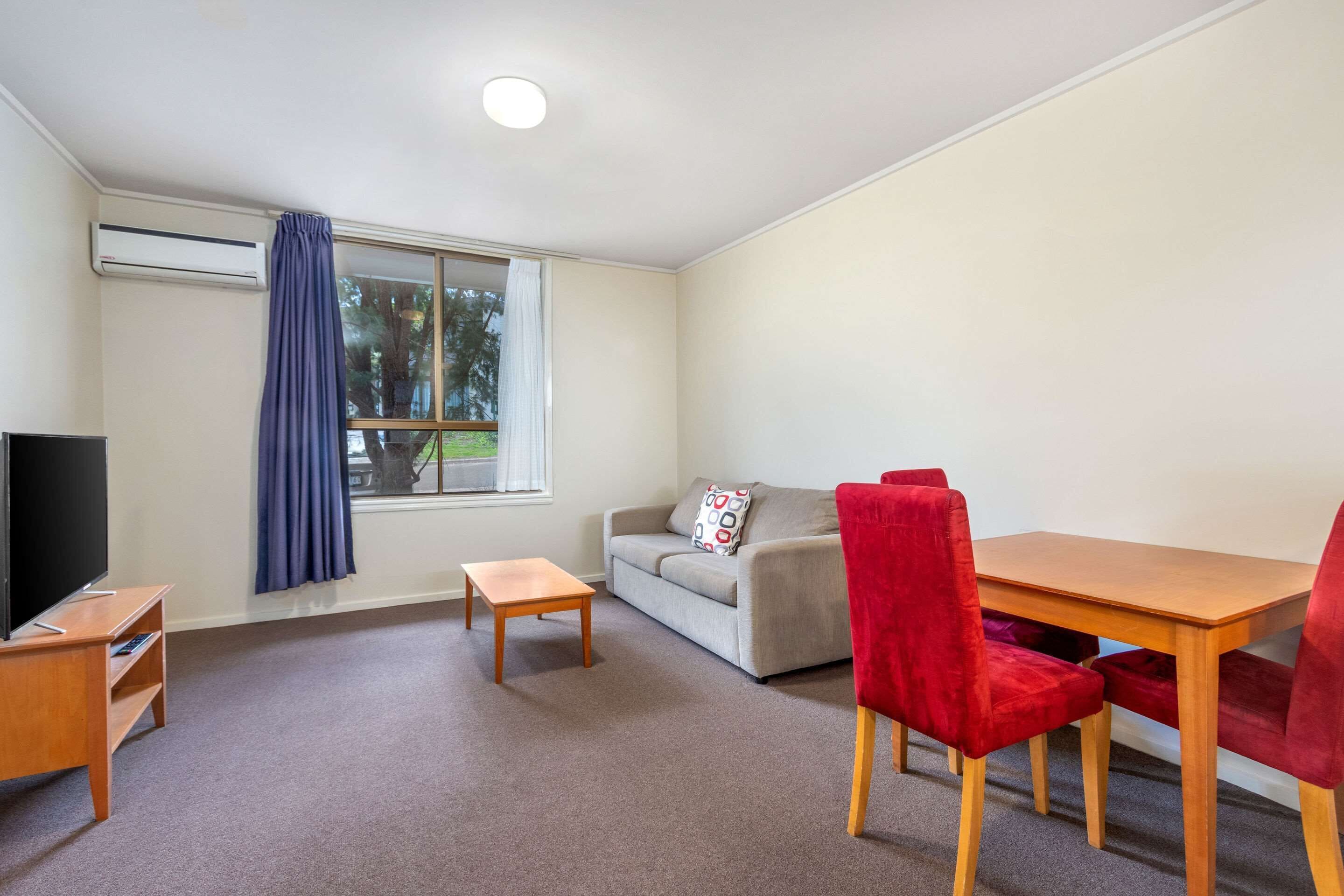 A room with a sofa, a table, a TV, and a window with curtains.