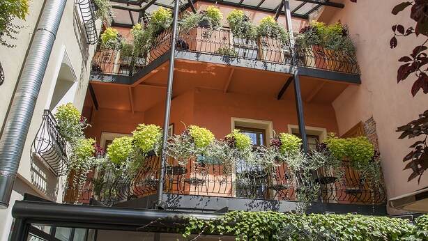 A multi-level outdoor cafe with tables and chairs, surrounded by balconies with plants. - Aparthotel Vicini dawniej Aparthotel Oberża (Kraków)