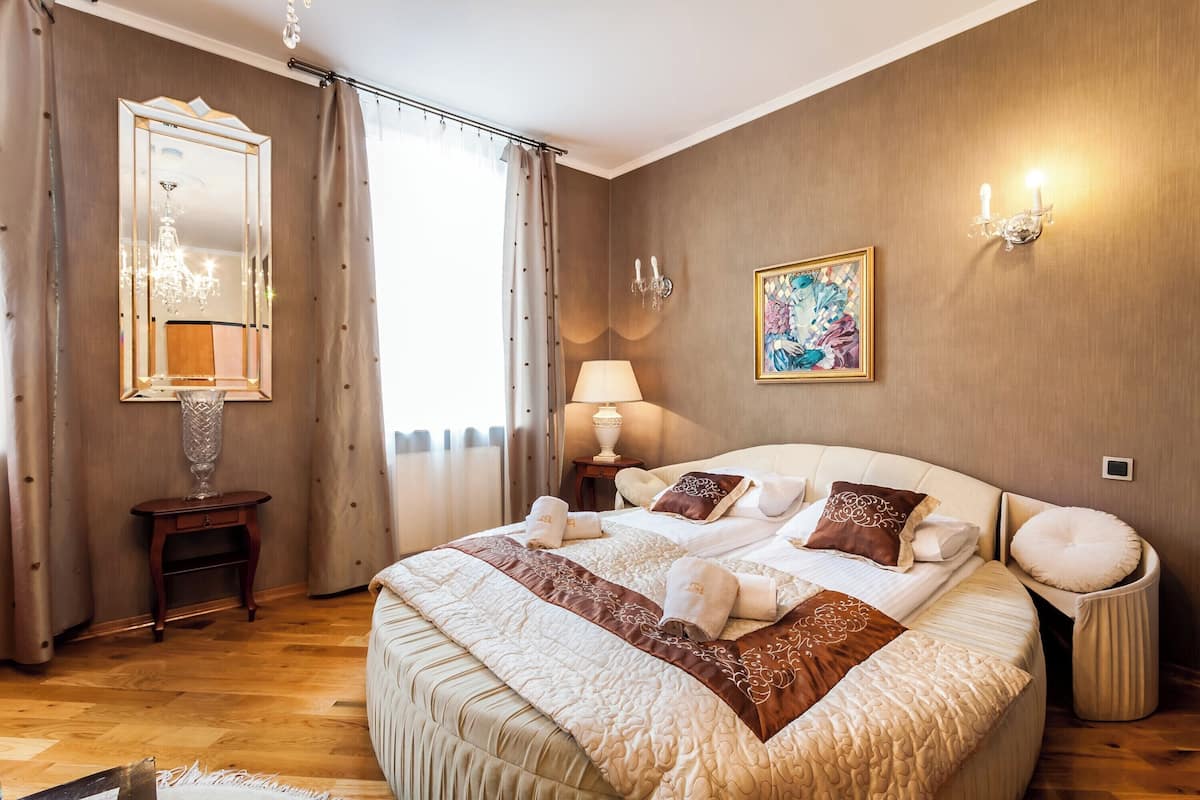 A bedroom with a large bed, a bedside table, a lamp, a mirror, and a painting on the wall.