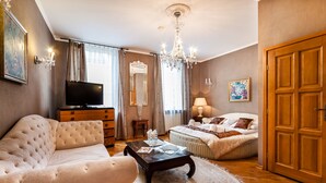 A spacious bedroom with a large bed, a sitting area with a sofa and coffee table, a television, and a chandelier. - Aparthotel Vicini dawniej Aparthotel Oberża (Kraków)