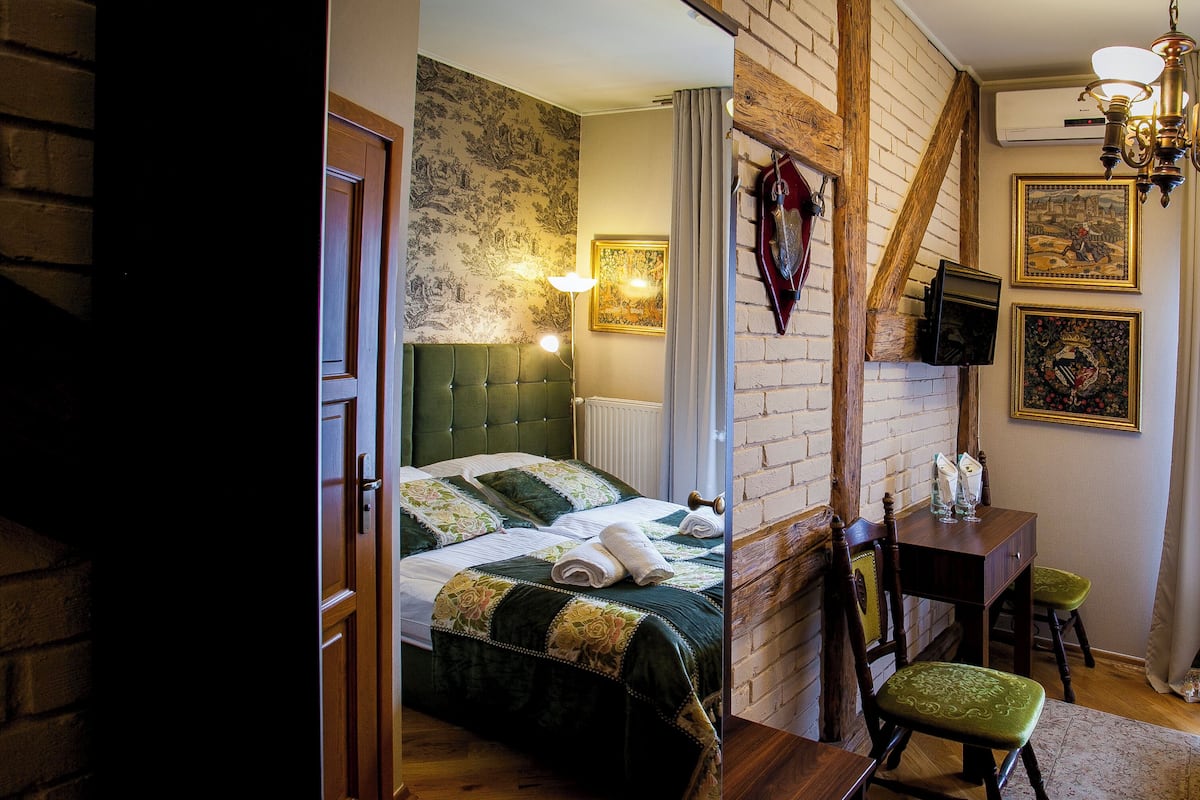A bedroom with a bed, a desk, a chair, a radiator, and a television.