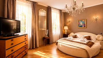 Une chambre d’hôtel avec un grand lit, un téléviseur posé sur une commode en bois, un lustre et un tableau accroché au mur.