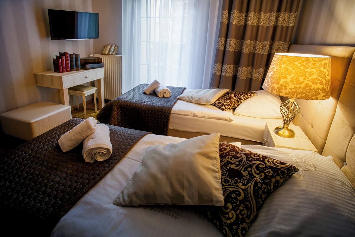 A hotel room with two beds, a desk, a TV, and a lamp.